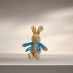 Peter Rabbit Pram Toy with a bright blue attachment clip resting on a soft cream blanket.