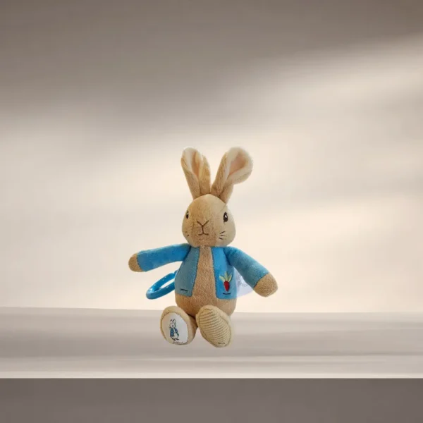 Peter Rabbit Pram Toy with a bright blue attachment clip resting on a soft cream blanket.