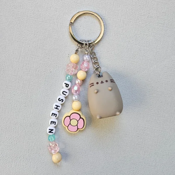 A cute gray Pusheen Tropical Vacation Keyring with pastel pink, yellow, and blue letter beads spelling PUSHEEN, attached to a durable silver ring.