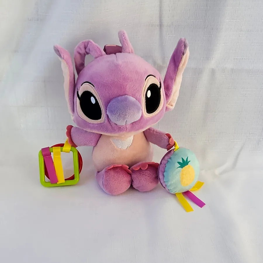 Disney-Baby-Angel-Activity-Toy-Front-View Plush Disney Baby Angel activity toy for infants, featuring a soft purple character doll with hanging plastic teething rings and a round plush pineapple rattle disc with satin tags.